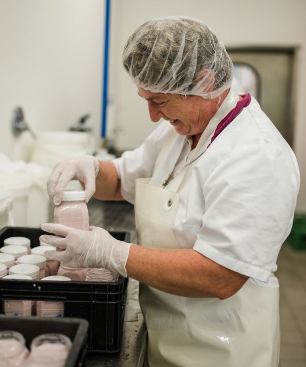 Mitarbeiterein in Hygienekleidung beim Abfüllen von Joghurt in der Molkerei