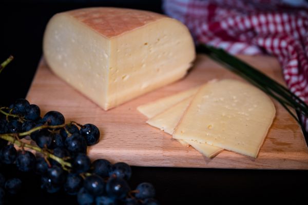 Ein viertel Käselaib und verschiedene Stückkäse auf einem Holzbrett auf der Wiese