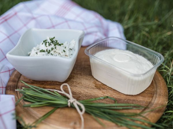 Ein Schälchen mit Frischkäse und ein Schälchen mit Kräuterquark auf einem Holzbrett auf der grünen Wiese